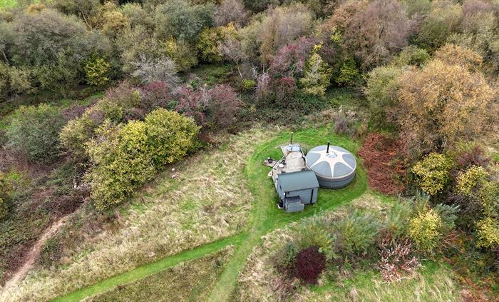 Bird's eye view of a green and beige yurt, with woodland and trees surrounding.